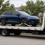 Blue electric SUV secured on a flatbed tow truck parked on a suburban street